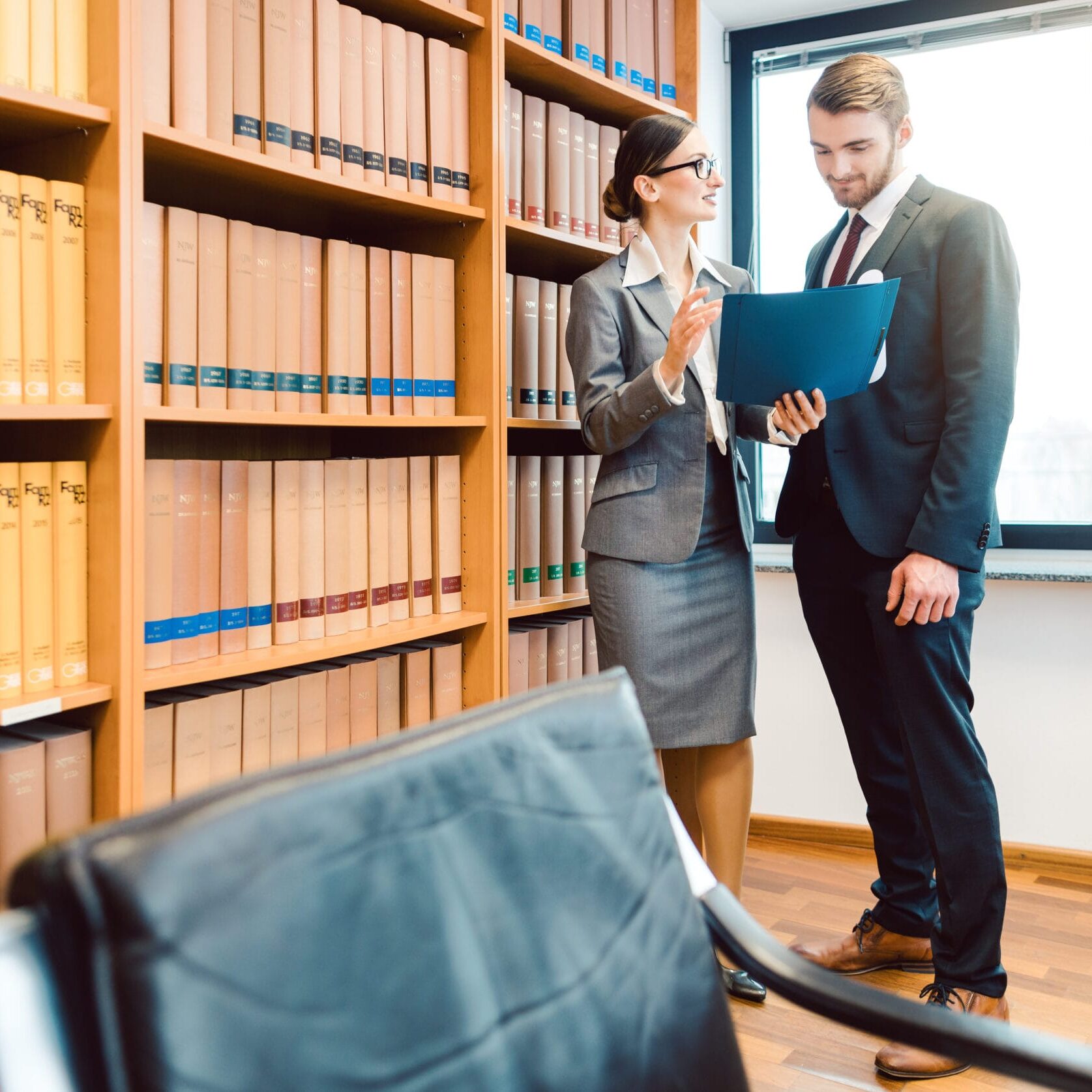 Lawyers in library of law firm discussing strategy in a case holding file Two lawyers in library of law firm discussing strategy in a case holding file