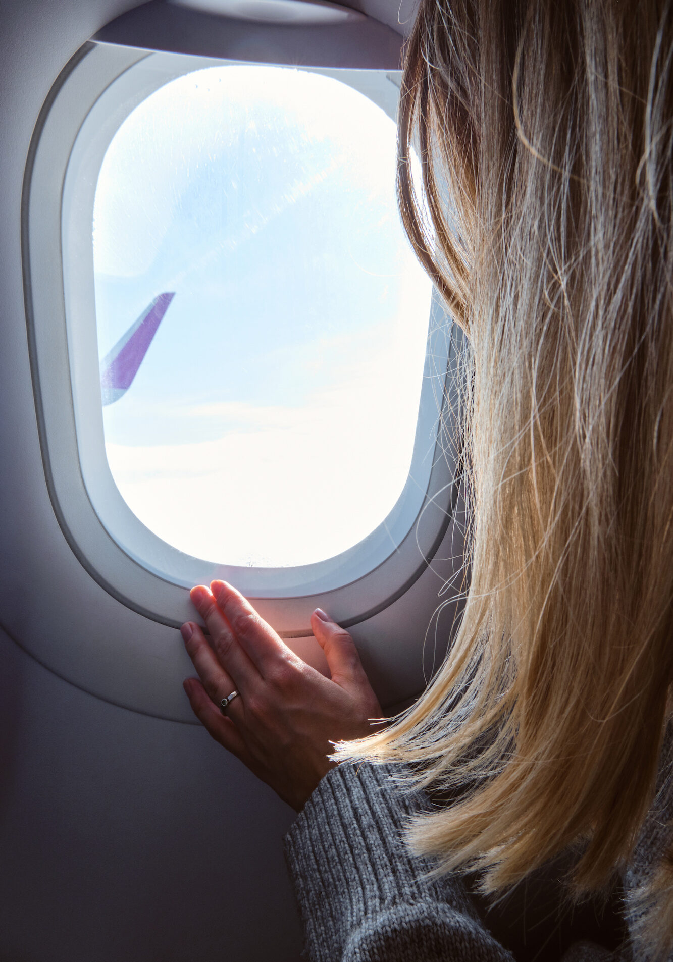 Woman looks out the window of an airplane. Hand near the porthole. Girl on the plane. Airplane wing, scenic view. Beautiful cloud, blue sky. Traveling by plane, adventure. Air transport. Aviation