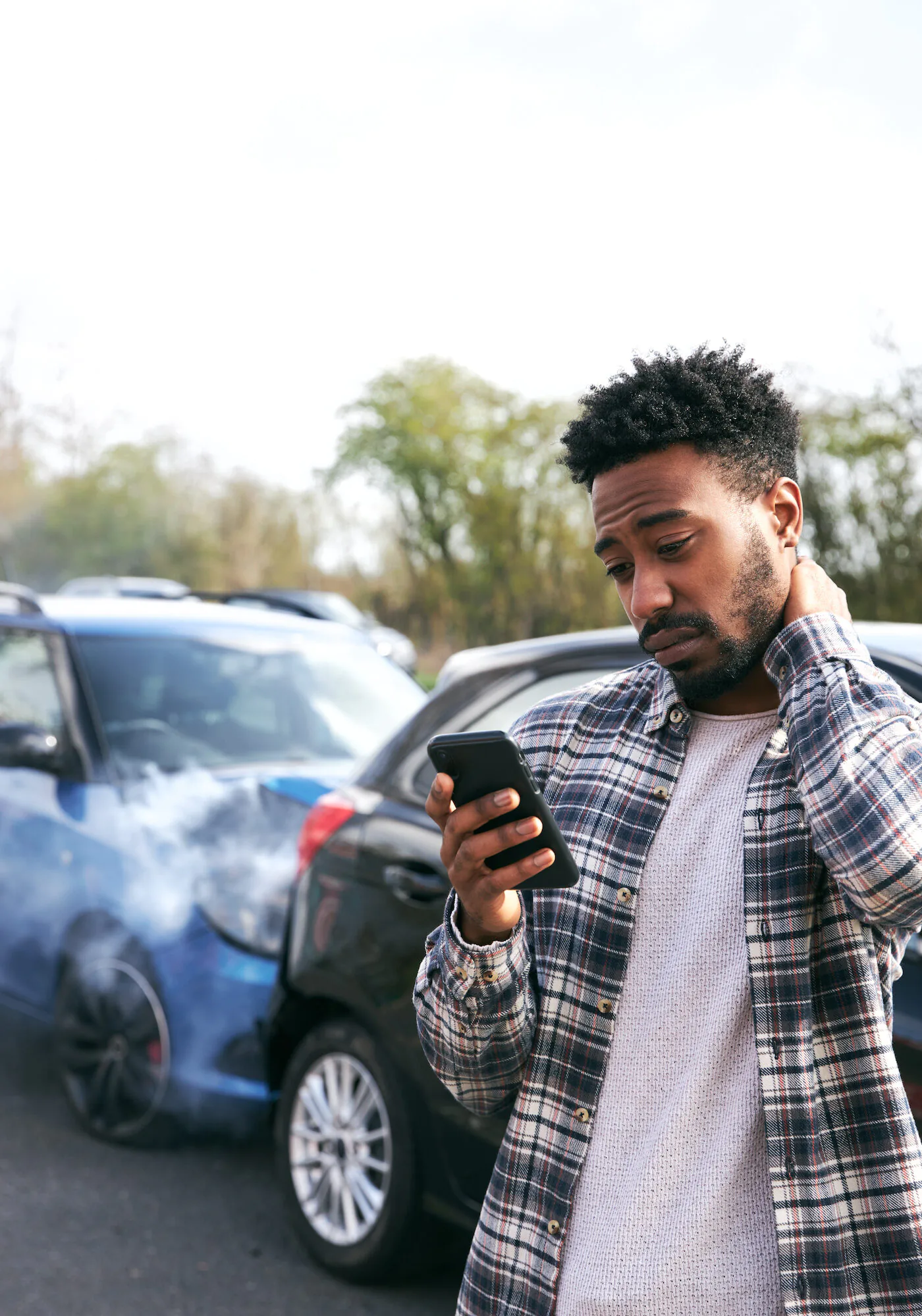 Male Driver With Whiplash Injury Calls Car Insurance Company On Mobile Phone After Traffic Accident Young male driver with whiplash injury standing by damaged car after traffic accident reporting incident to insurance company using mobile phone