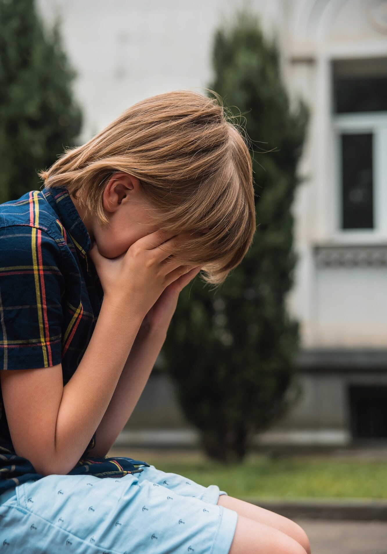 Child abuse. Child need help. Violence concept. Boy sitting on a bench covered his face with his hands Child abuse. Child need help. Violence concept. Boy sitting on a bench covered his face with his hands
