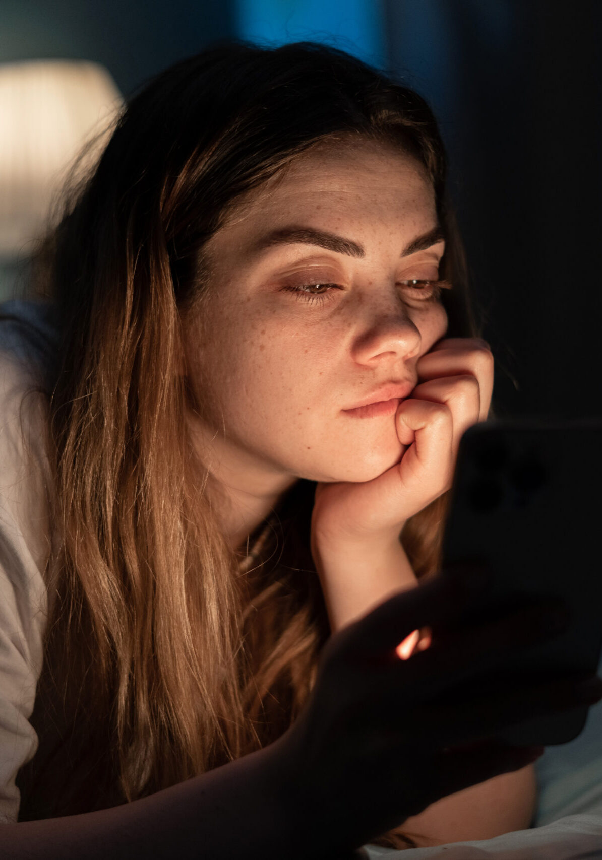 Addicted young woman chatting and surfing on the Internet with smartphone late at night in bed. Insomnia and mobile addiction concept.
